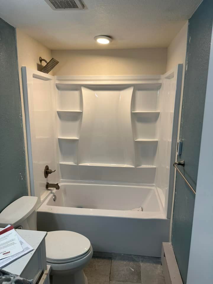 A bathroom with a toilet , bathtub , shower and shelves.