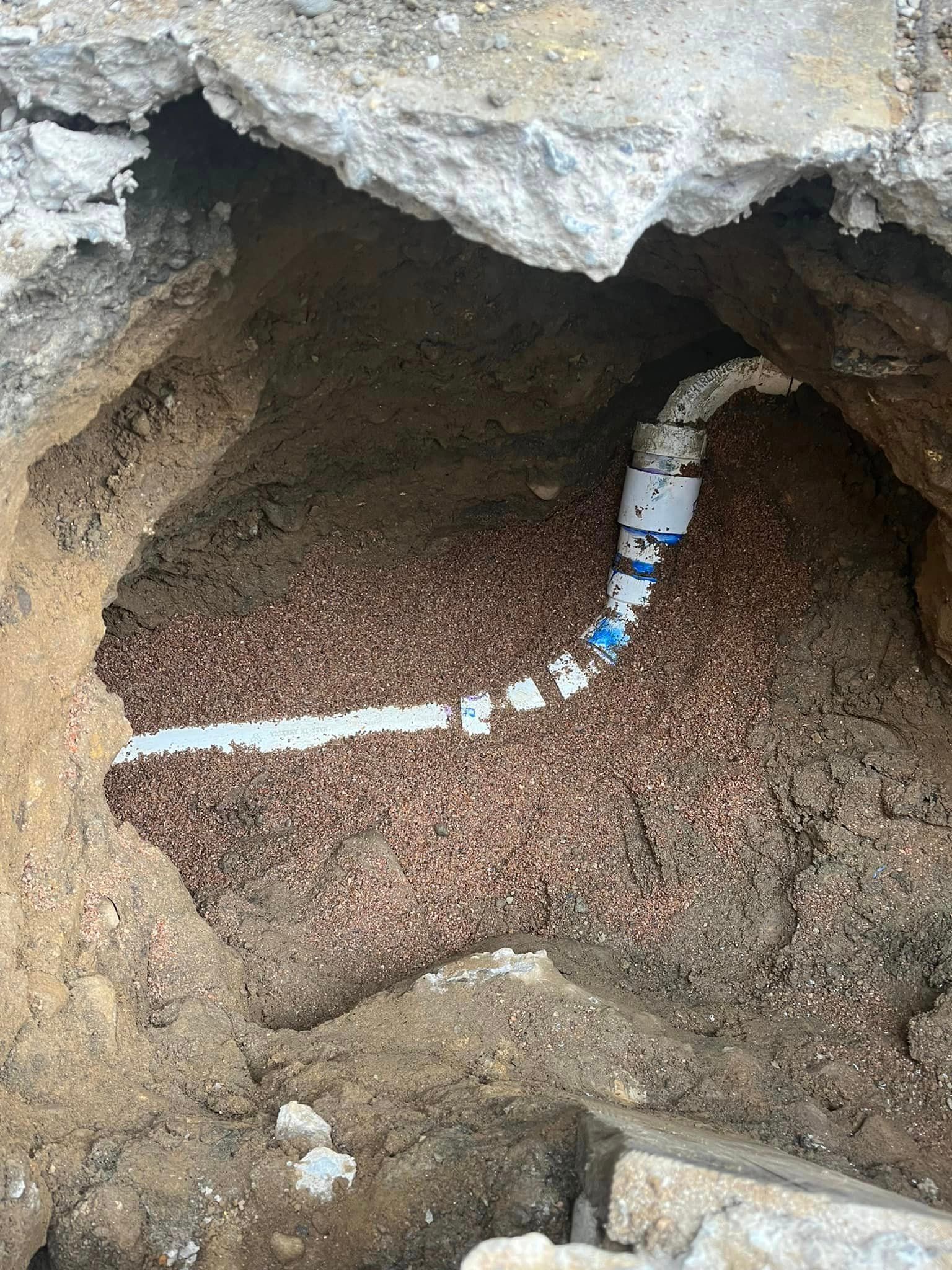 A pipe is laying in the dirt in a hole.