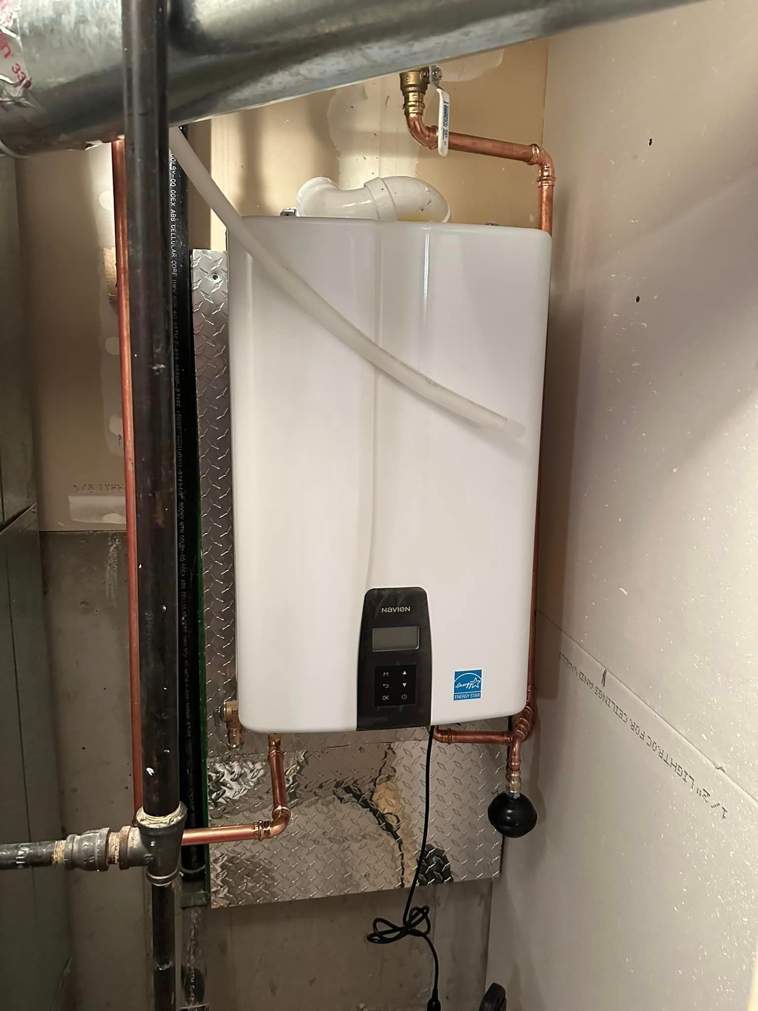 A white water heater is hanging on a wall next to copper pipes.