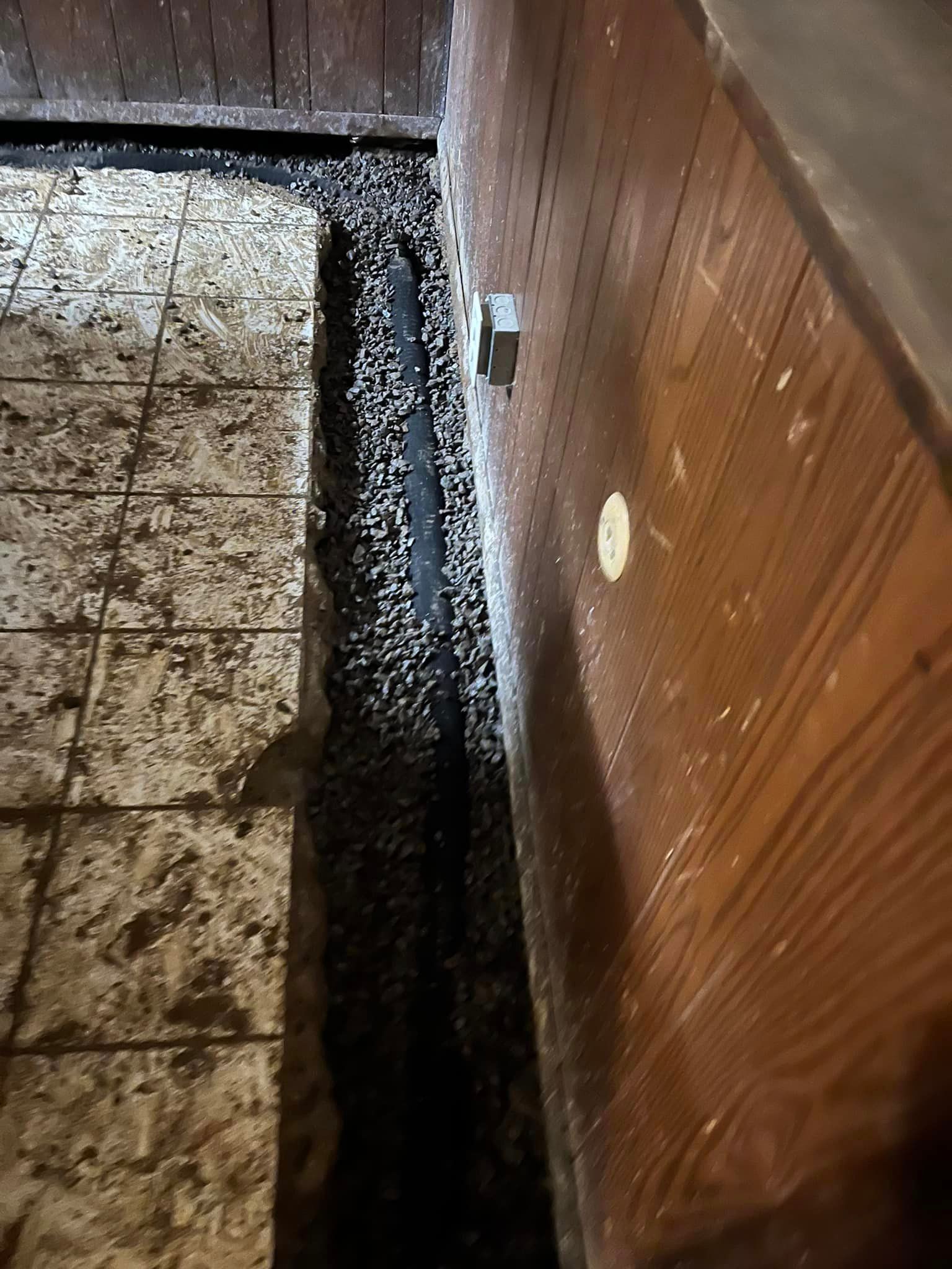 There is a hole in the floor next to a wooden wall.