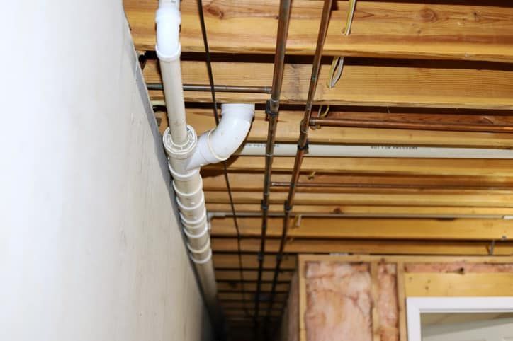 A white pipe is hanging from the ceiling of a basement.