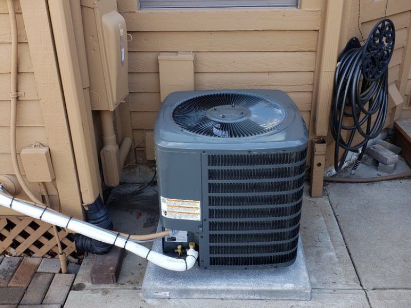 An air conditioner is sitting outside of a house next to a hose