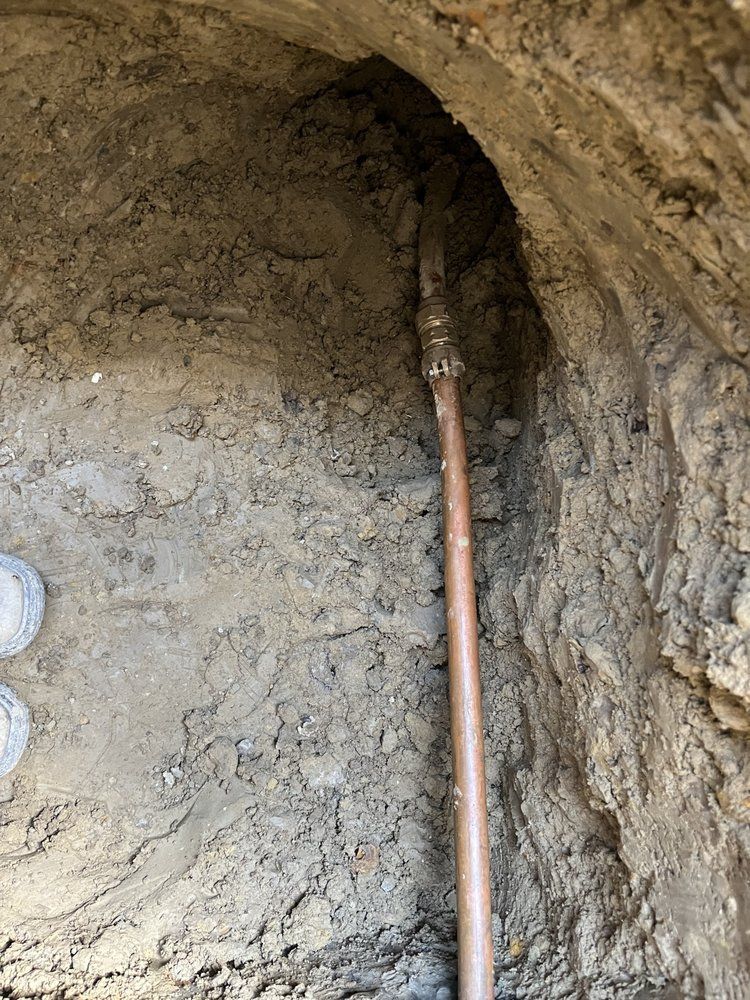 A copper pipe is laying in the dirt in a hole.