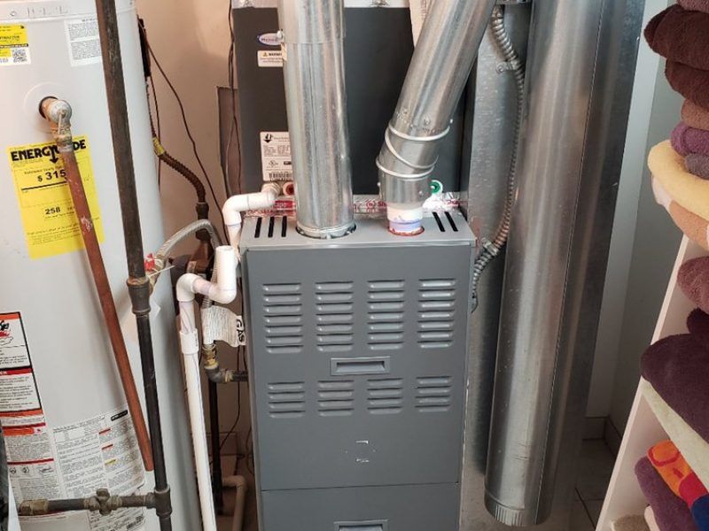 A furnace is sitting in a room next to a water heater.