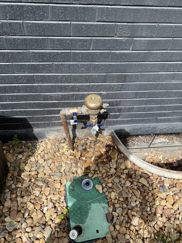 A water meter is sitting on top of a pile of rocks next to a brick wall.