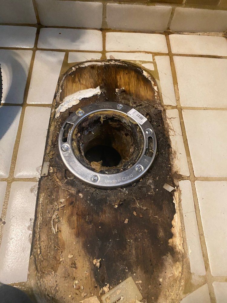 A toilet is sitting on a tiled floor with a hole in it.