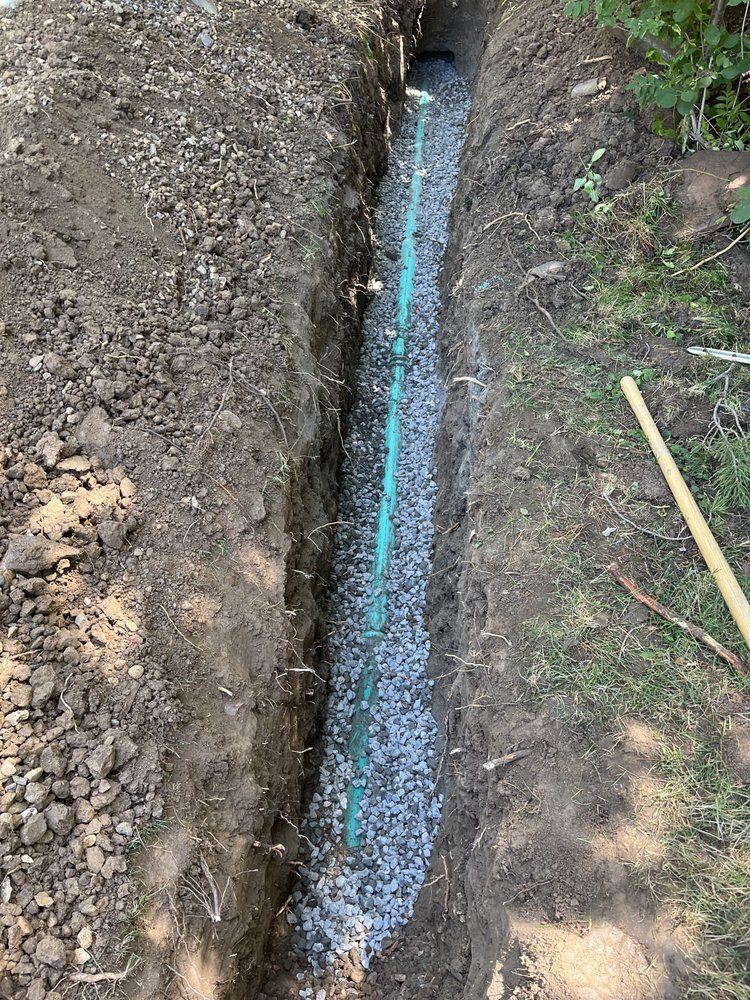 A green pipe is being installed in a trench.