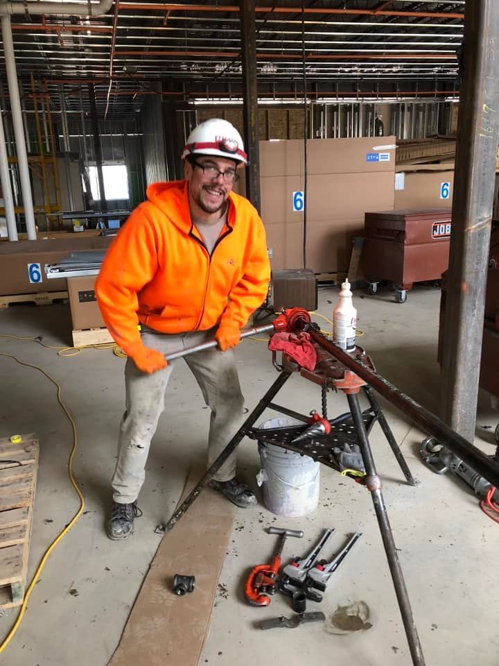 TCF Emergency Plumbing & Heating - A man in an orange jacket is standing next to a pipe clamp in a room.