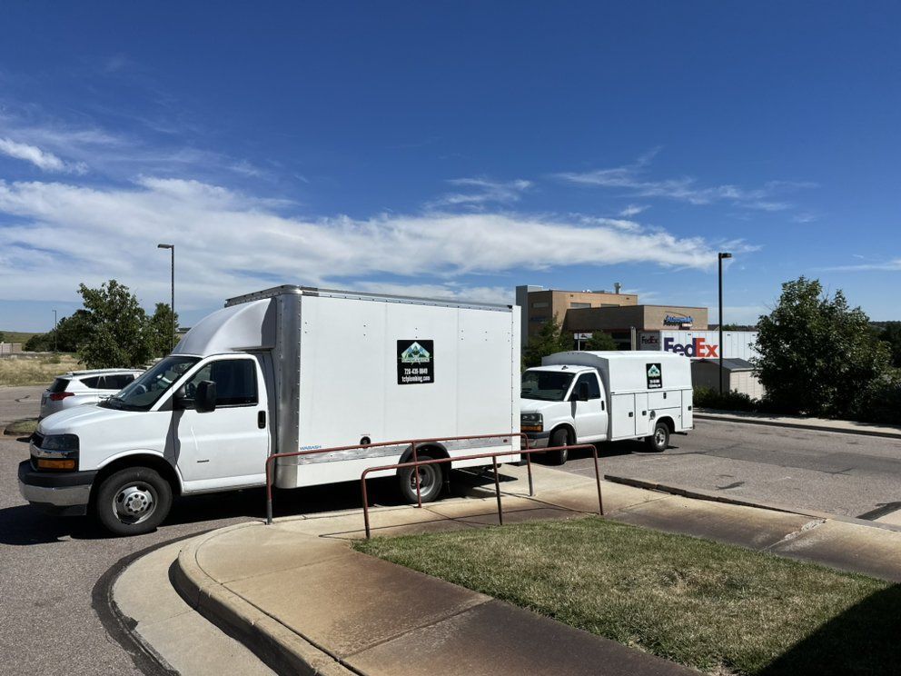 Two white trucks are parked on the side of the road in front of a fedex building.