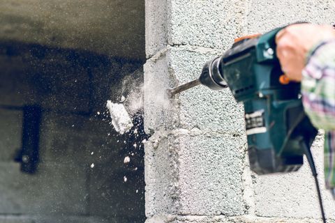 A person is using a hammer drill to drill a hole in a brick wall.