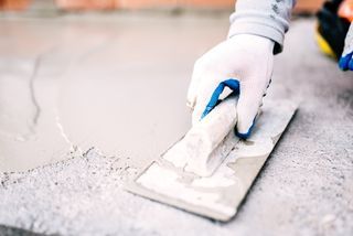 A person is using a trowel to spread concrete on the ground.