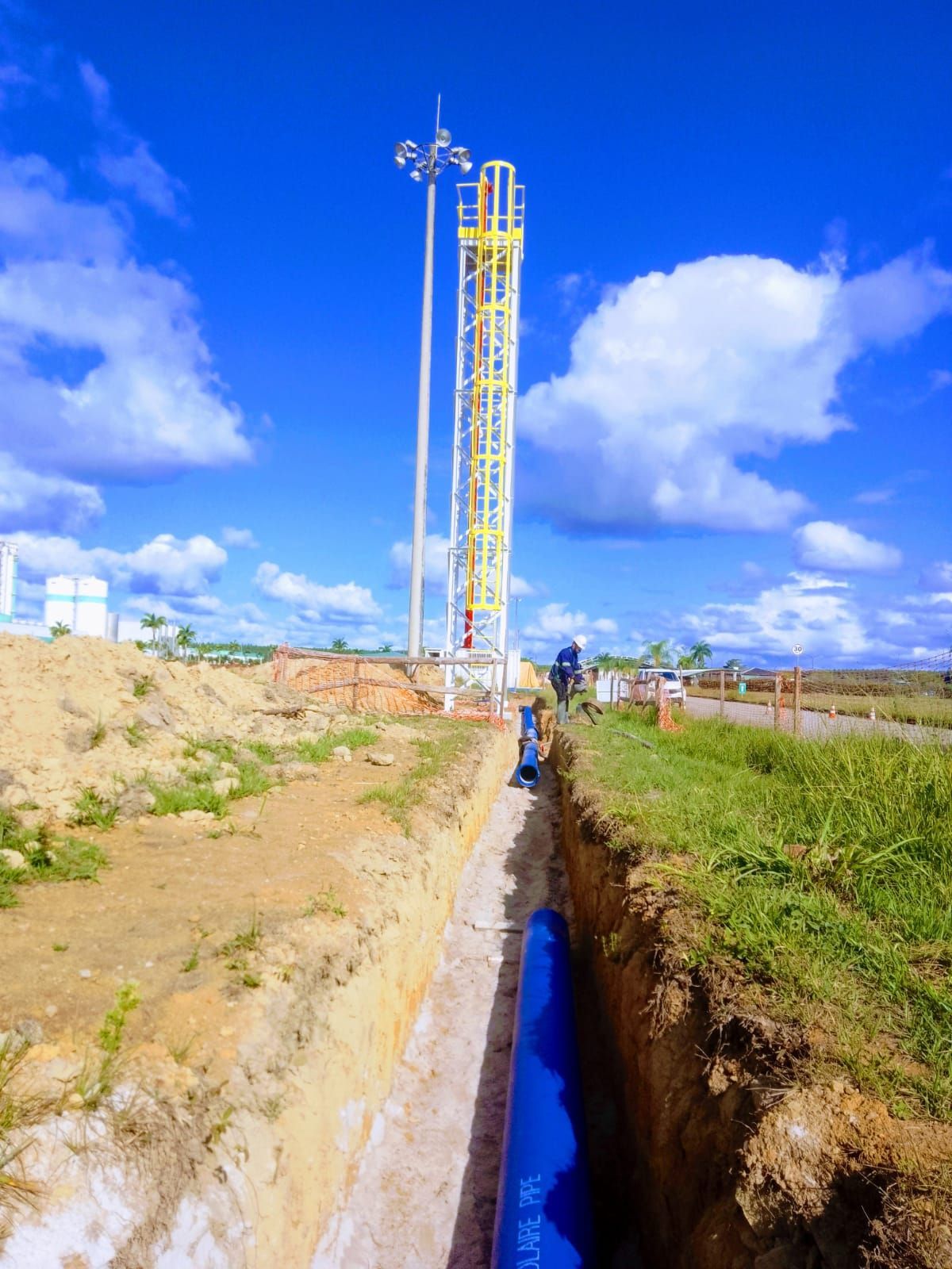 Um tubo azul está sendo instalado em uma vala próxima a uma torre.