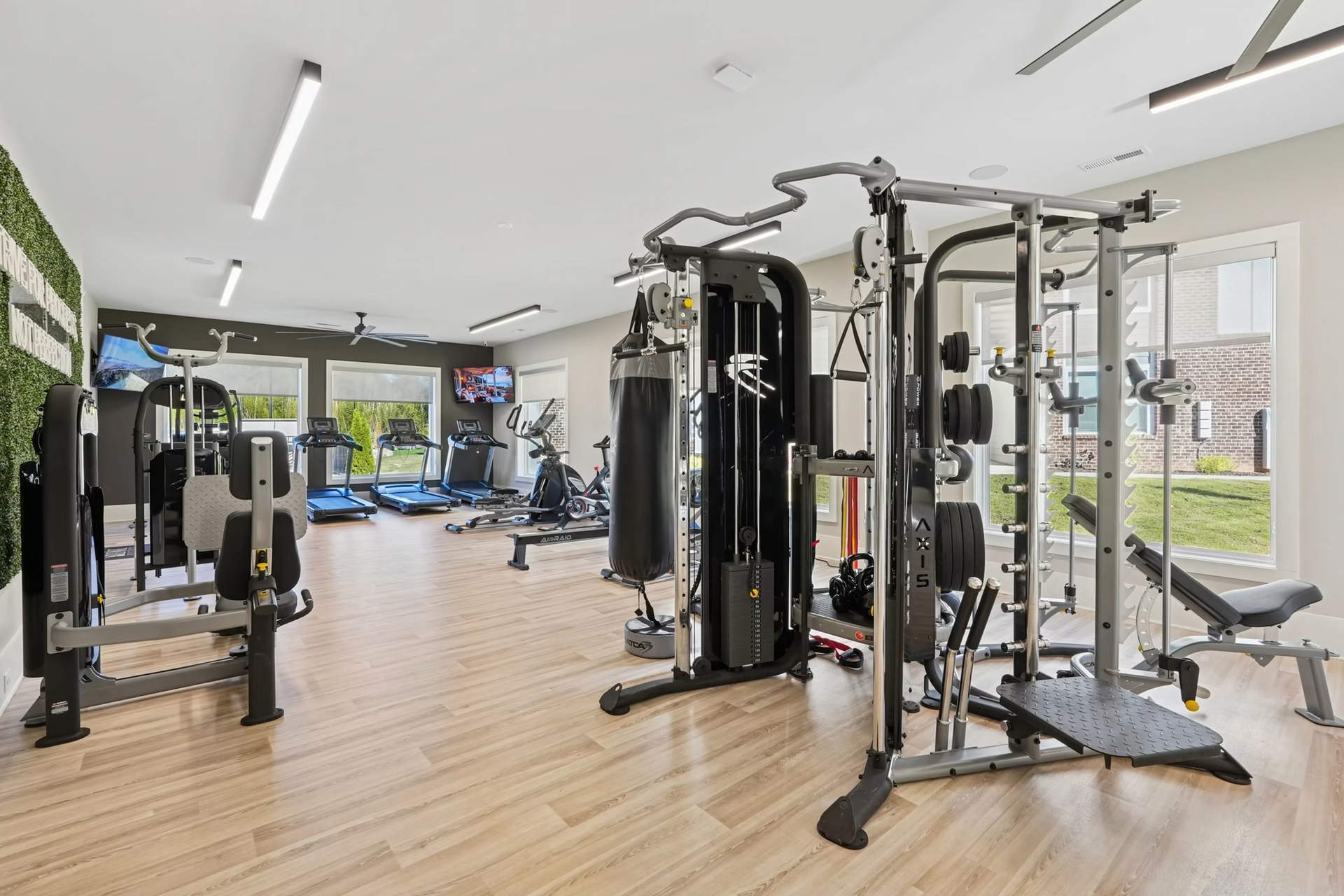 Bright modern gym with exercise machines, wood floors, and large windows overlooking greenery