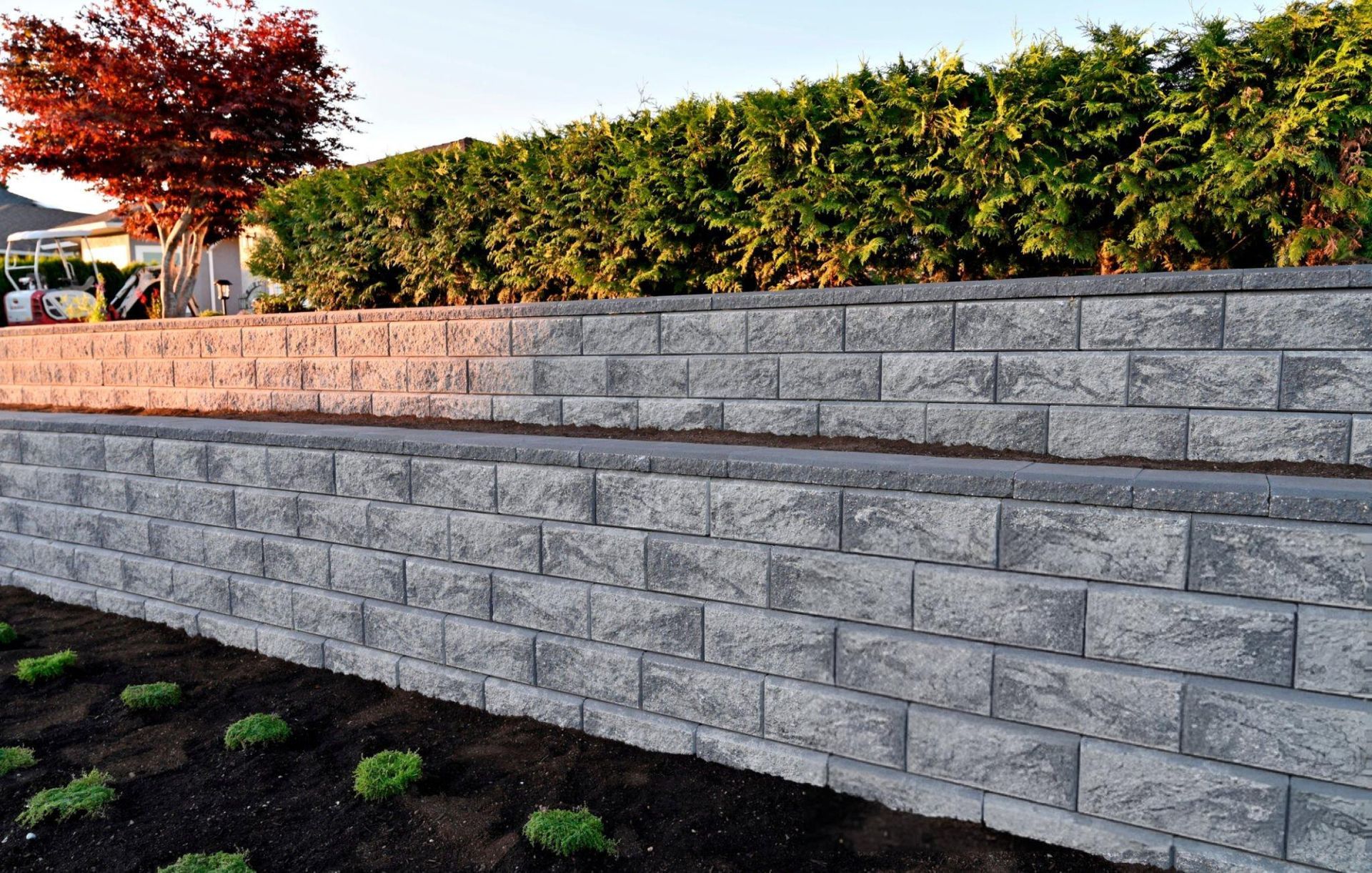 A close-up capture of a gray block stone retaining wall built as a two-tier wall into a landscape.
