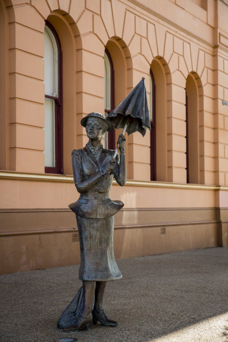A Statue of a Woman Holding an Umbrella in Front of a Building — MDK Mini Excavator - Dingo & Tipper Hire in Maryborough, QLD