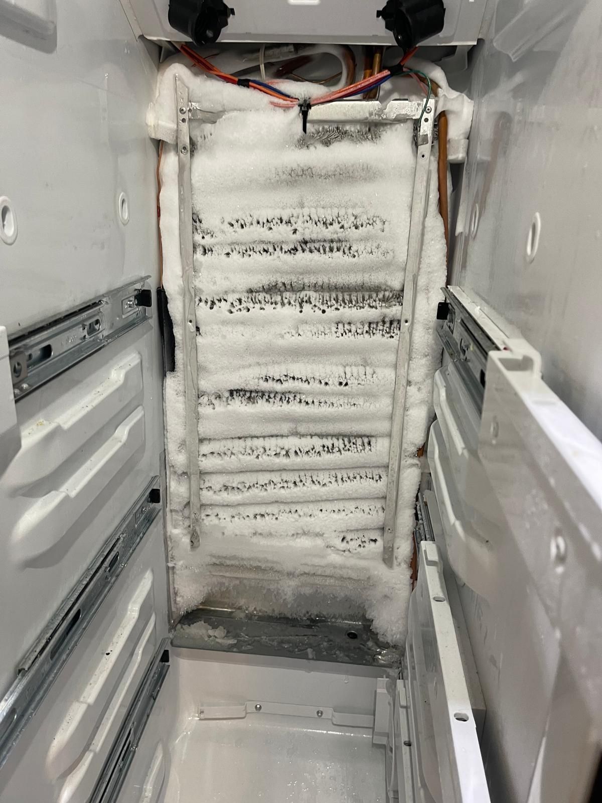 Interior of a freezer compartment heavily covered in ice and frost, showing coils and metal structures.