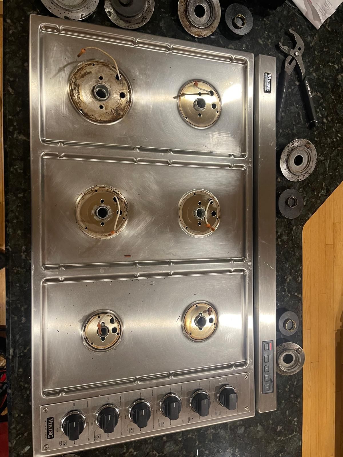 Stainless steel gas cooktop with burners removed for cleaning.