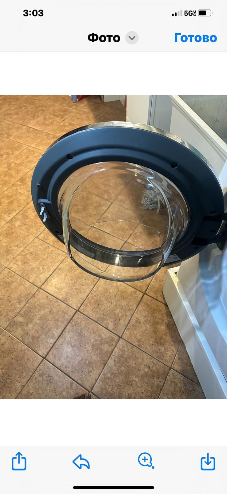 Open washing machine door with a clear, cracked glass. Brown tiled floor.