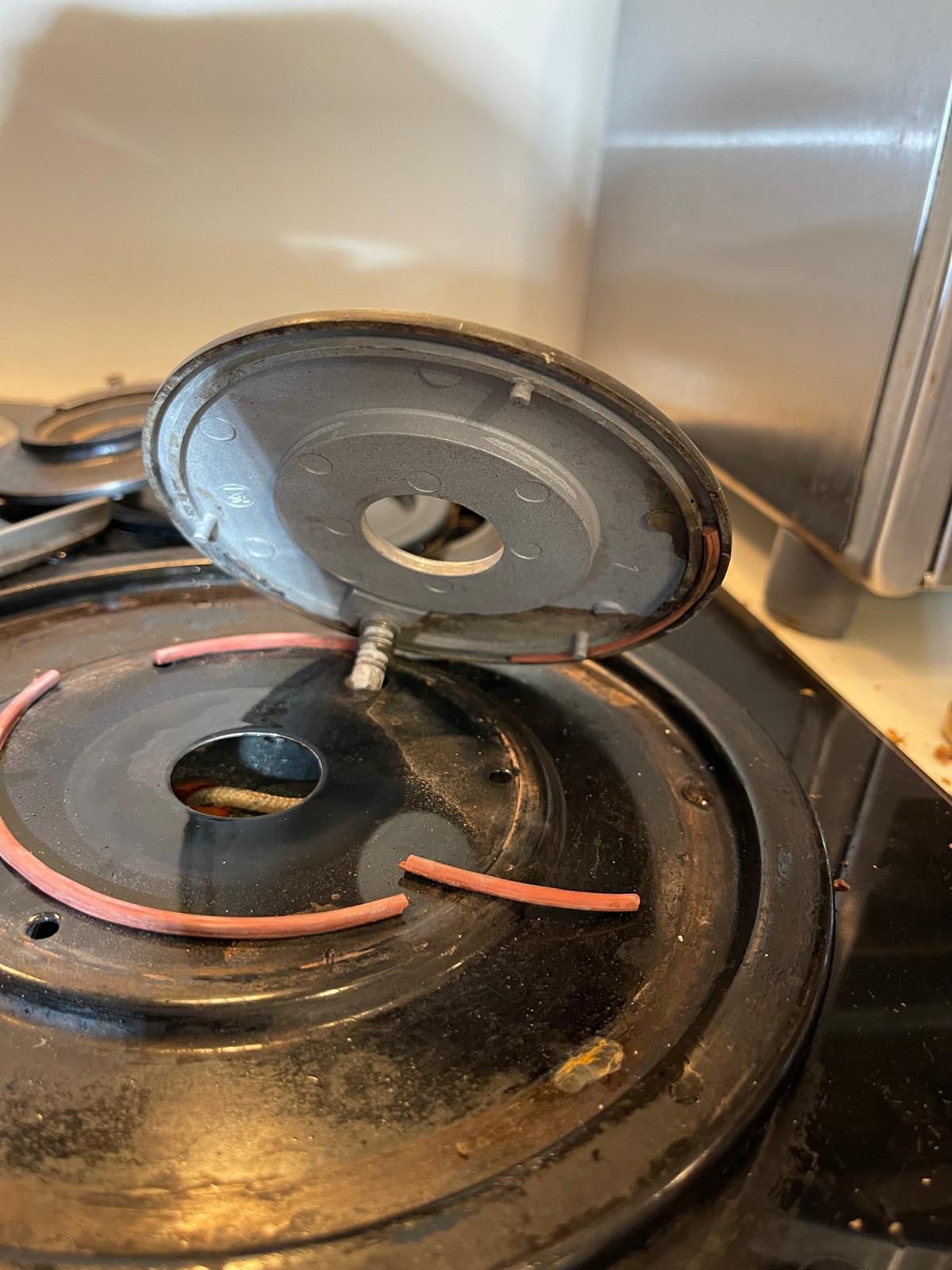 Black stove burner with detached lid, revealing a small tube and pink rubber seals.