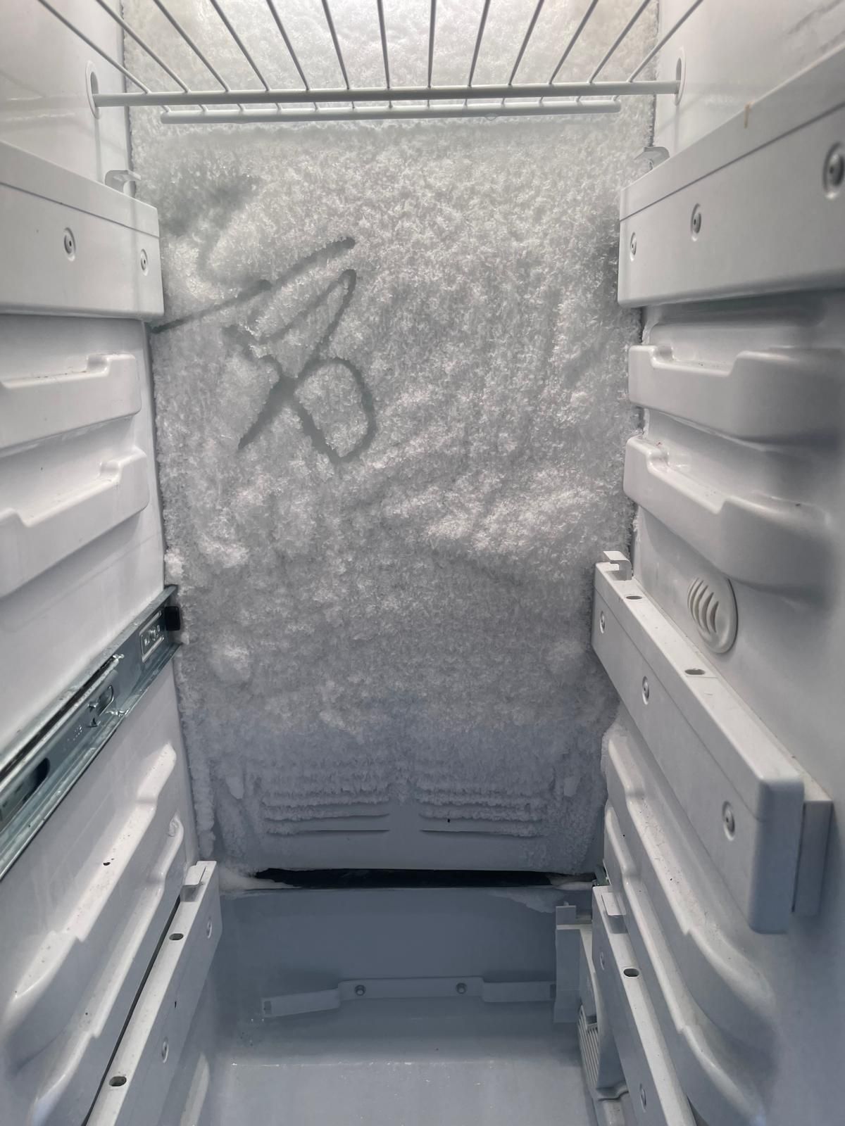 Interior view of a freezer covered in thick ice, showing the open door and wire rack.