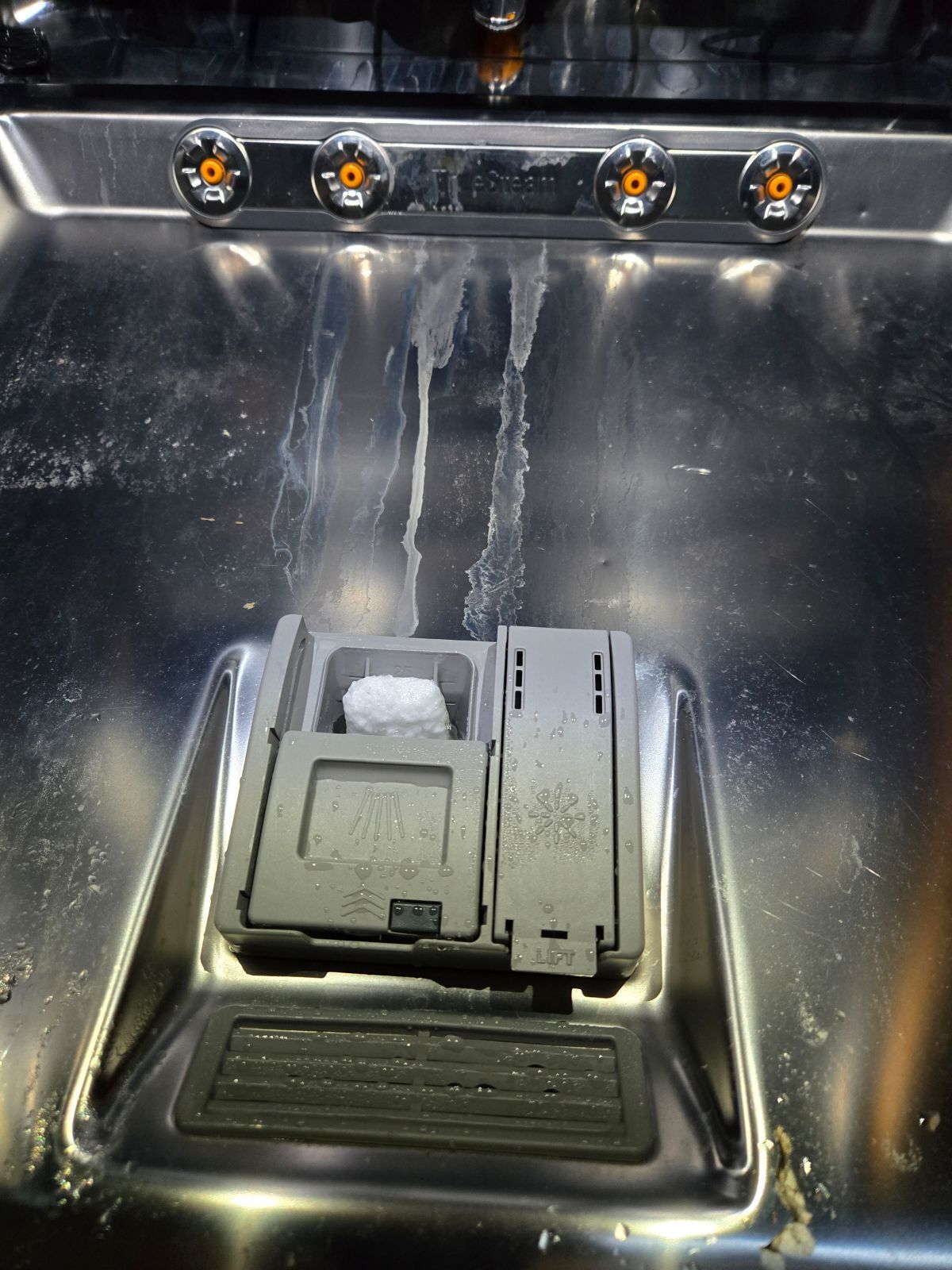 Open dishwasher detergent dispenser with undissolved tablet.