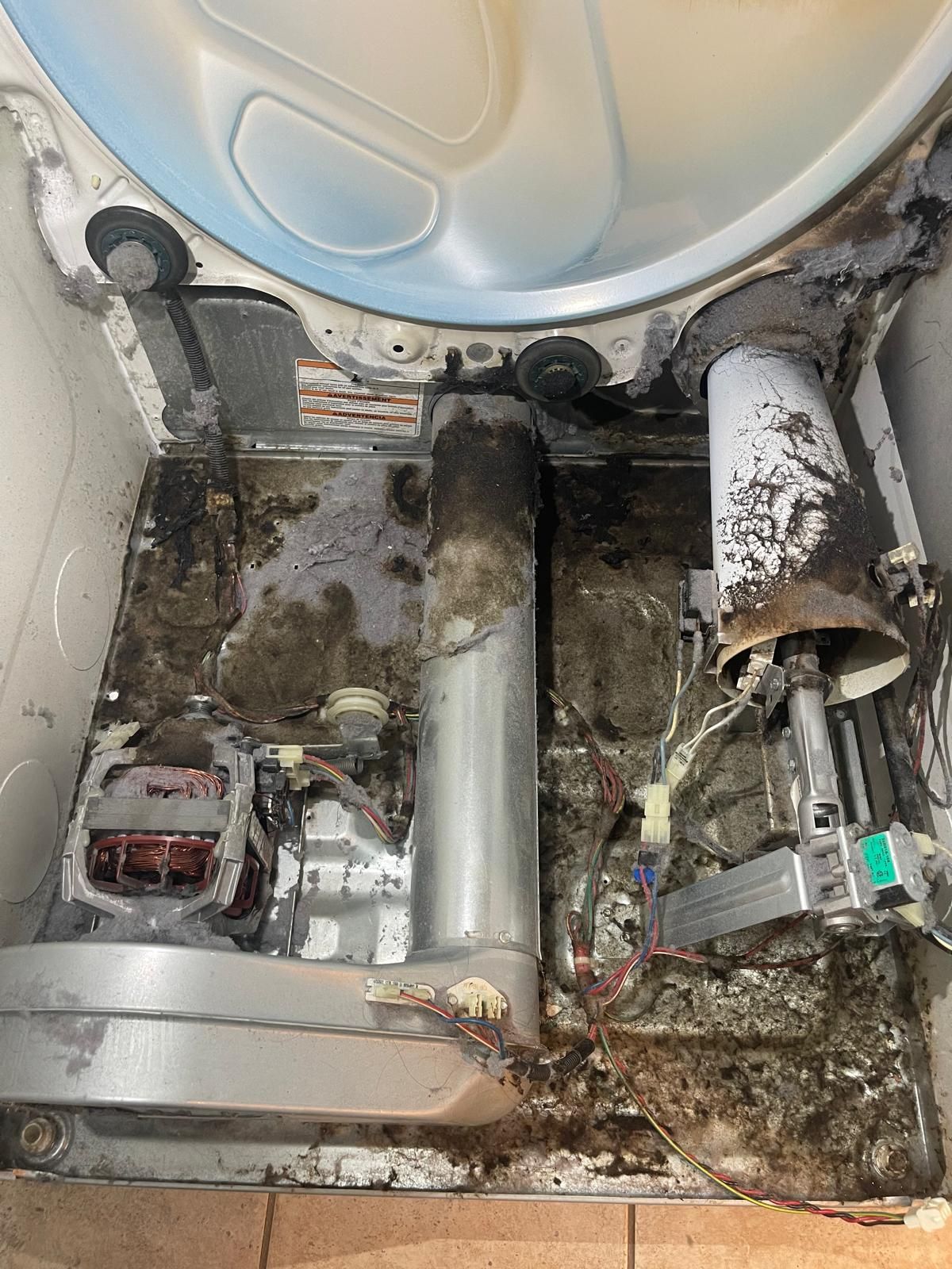 Inside of a dirty dryer with lint buildup and some burnt debris around the heating element and motor.