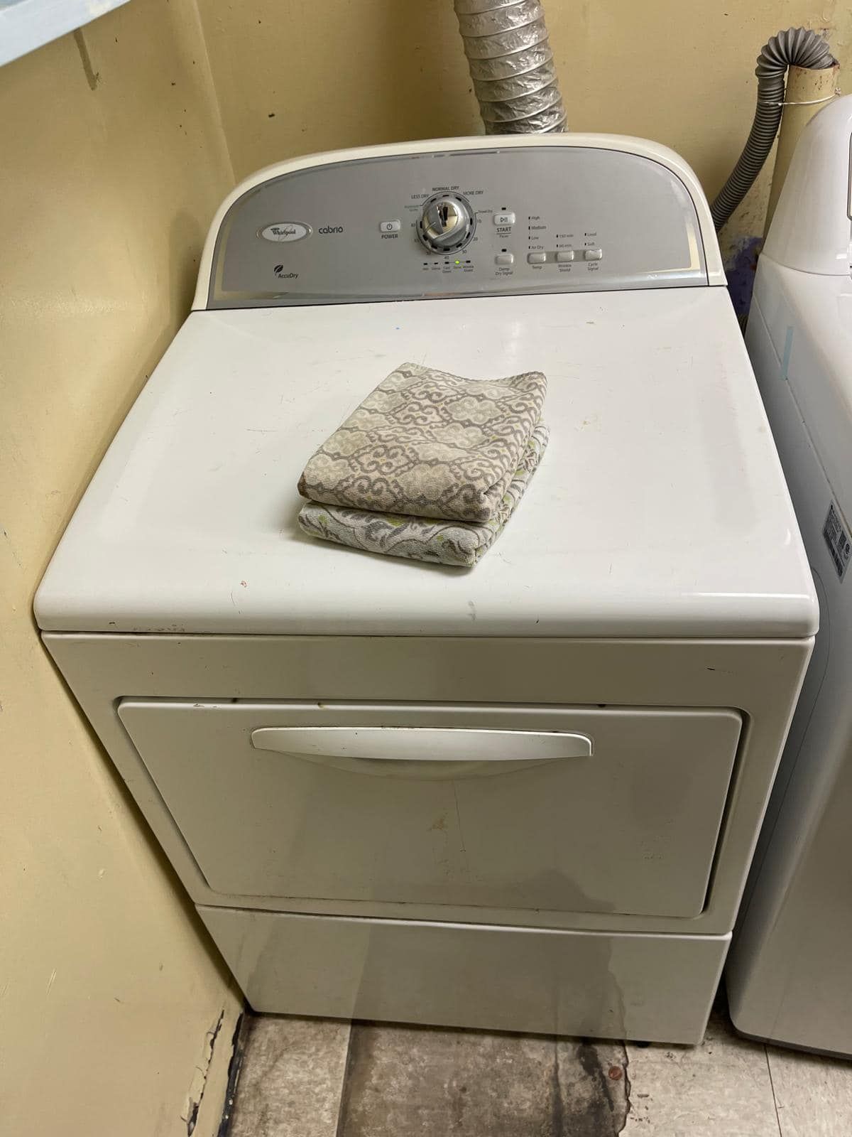 White Whirlpool dryer with folded towels on top, in a laundry room.