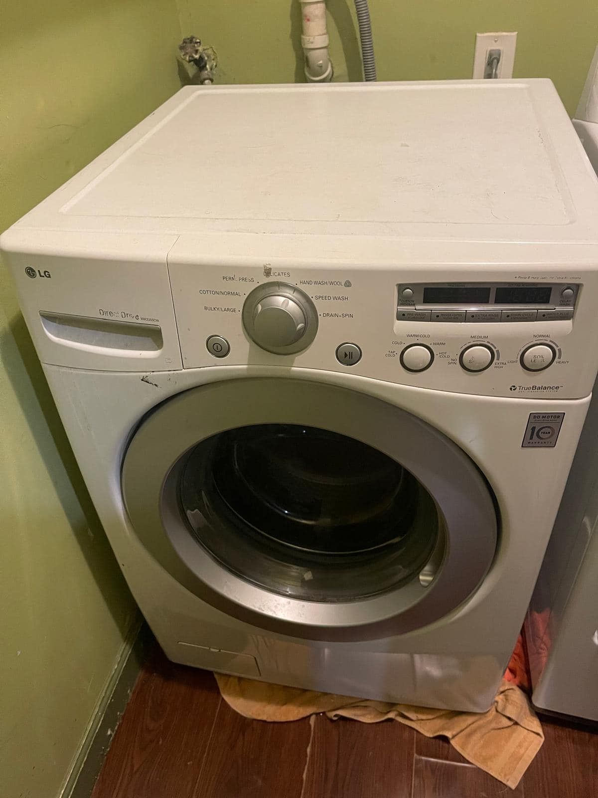 Front-loading LG washing machine, white with a silver door, set against a green wall and brown floor.
