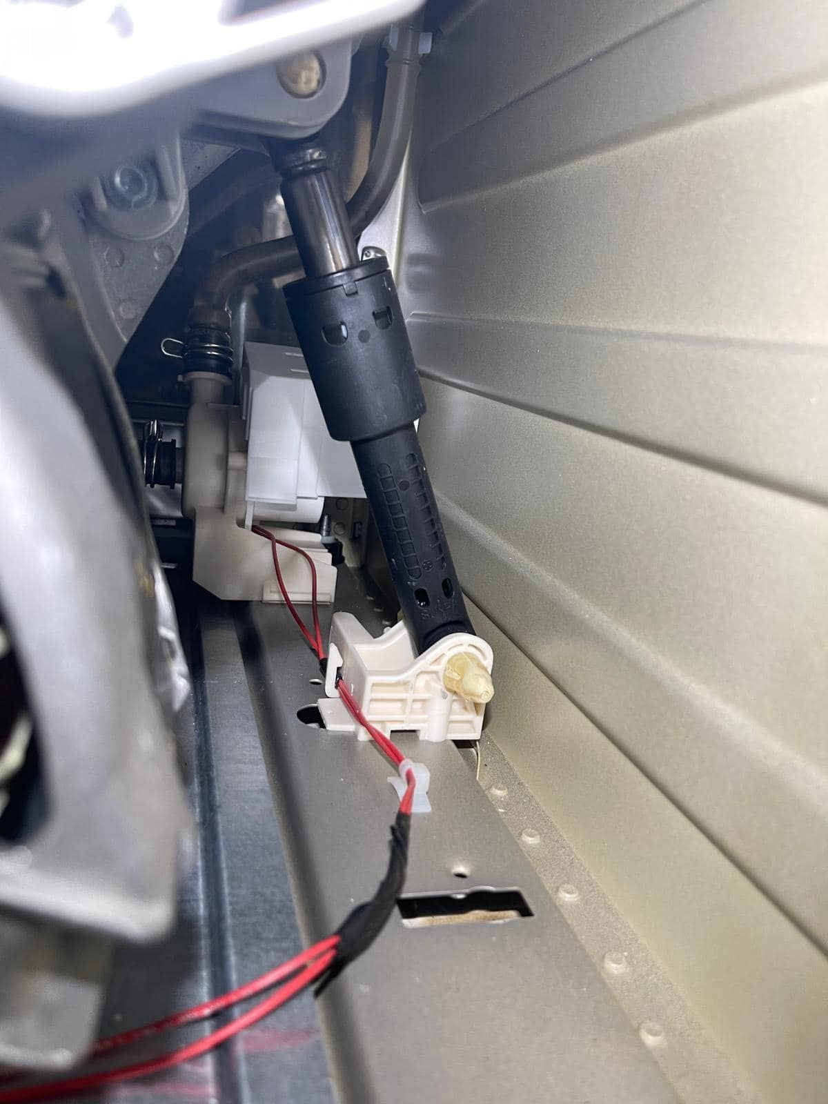 A close-up of a washing machine interior with a black shock absorber and connected wires.