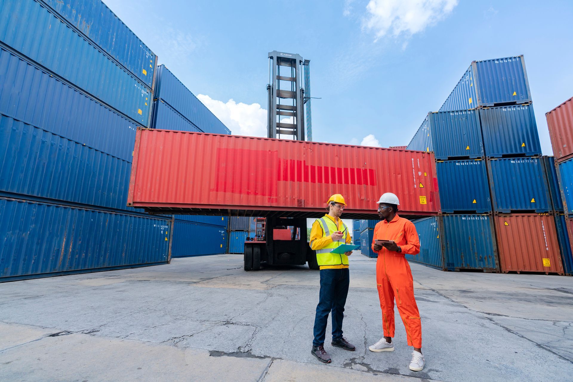 Two workers are seen in front of commercial storage containers at a port.
