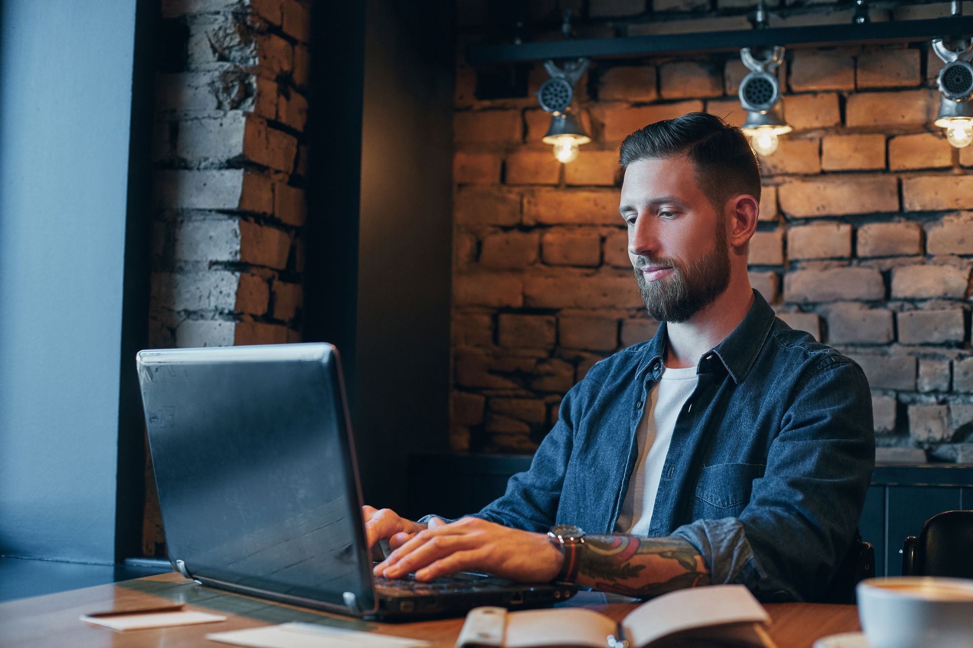 Homem branco com jaqueta azul sentado em frente ao notebook.