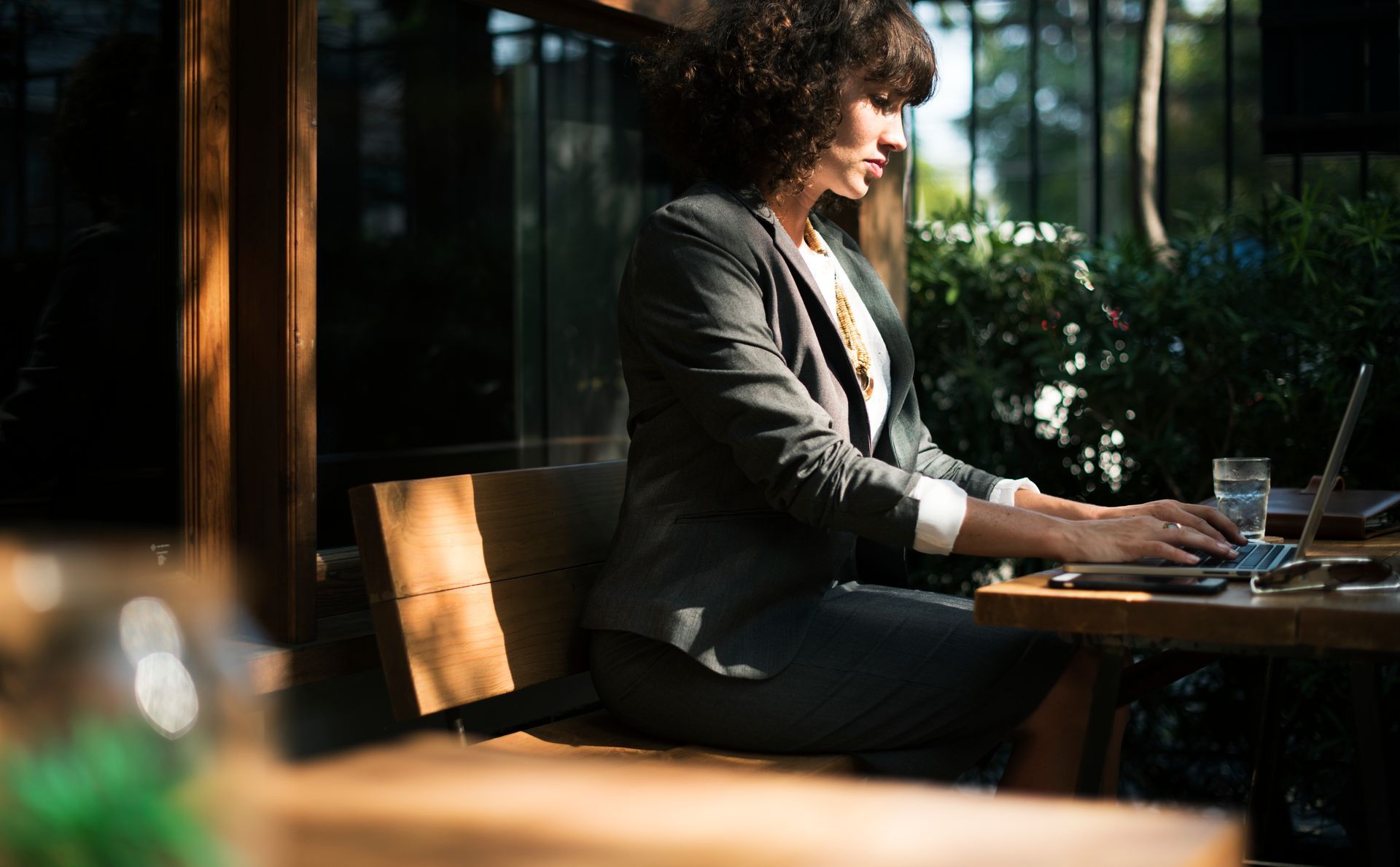 Woman in business suit, working on laptop at outdoor table.
