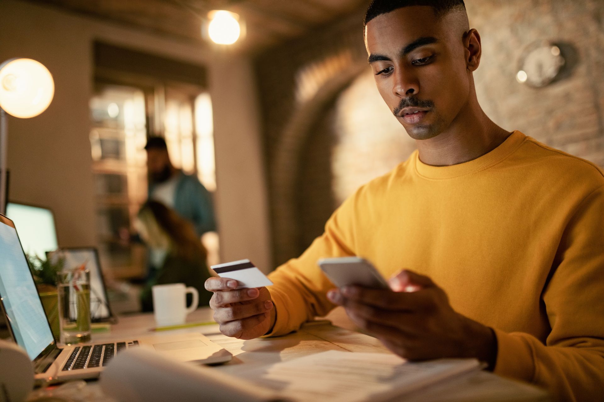 Jovem negro olhando para o celular e cartão de crédito