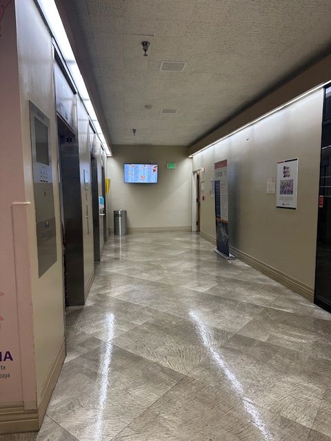 Hallway with elevators, a digital display, and a poster, with tiled floor.