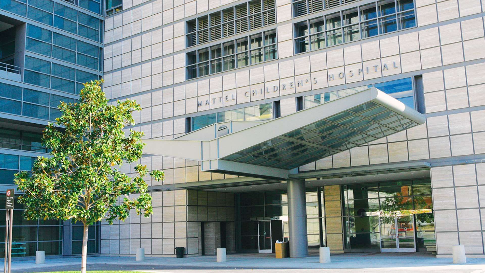Main entrance of a large medical building with glass windows and street in front.