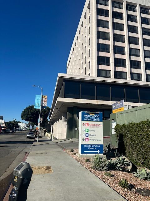 Exterior of Cedars-Sinai Medical Center building with directional sign on a sidewalk under a blue sky.