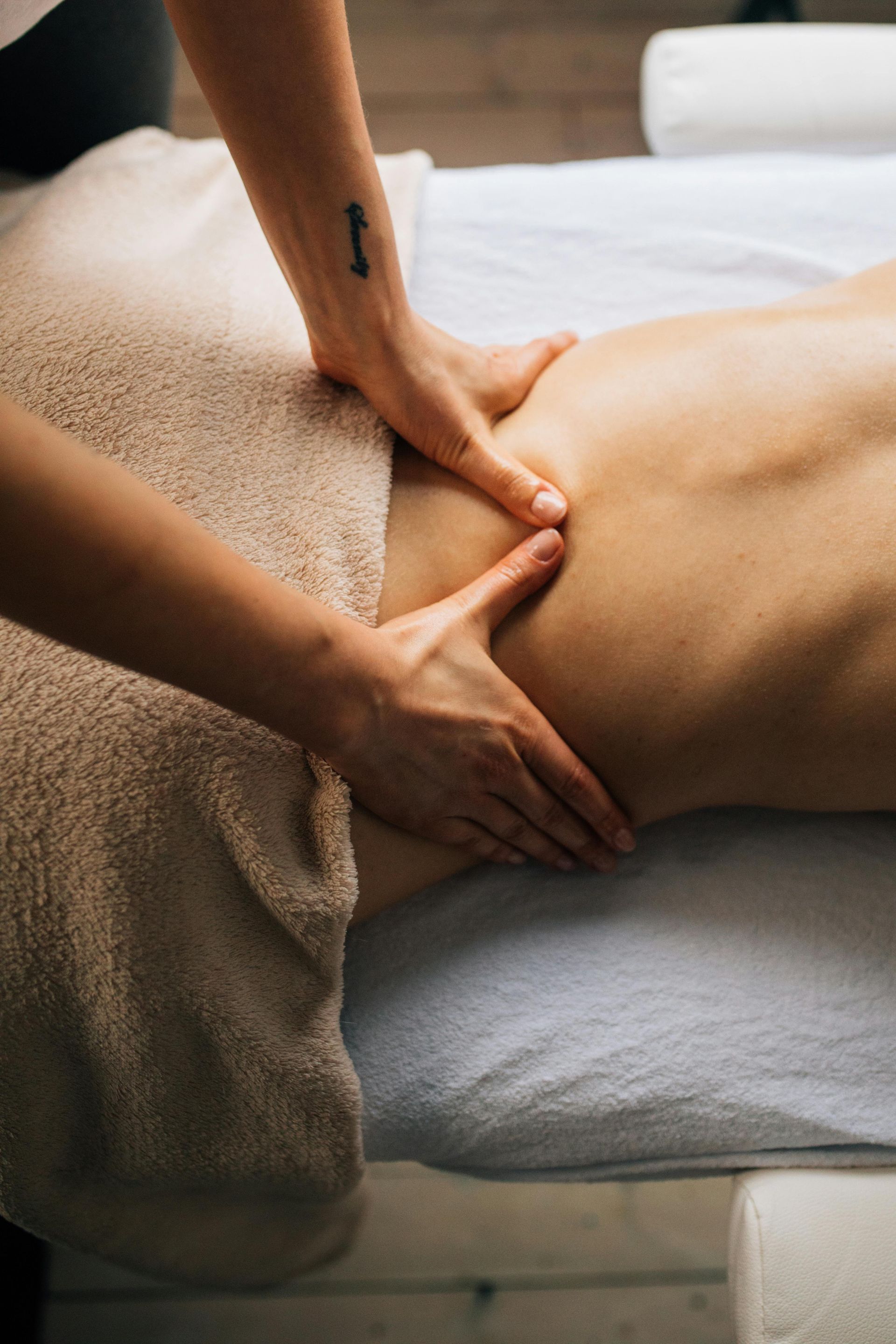 Hands massaging a person's back on a massage table, partially covered by a towel.