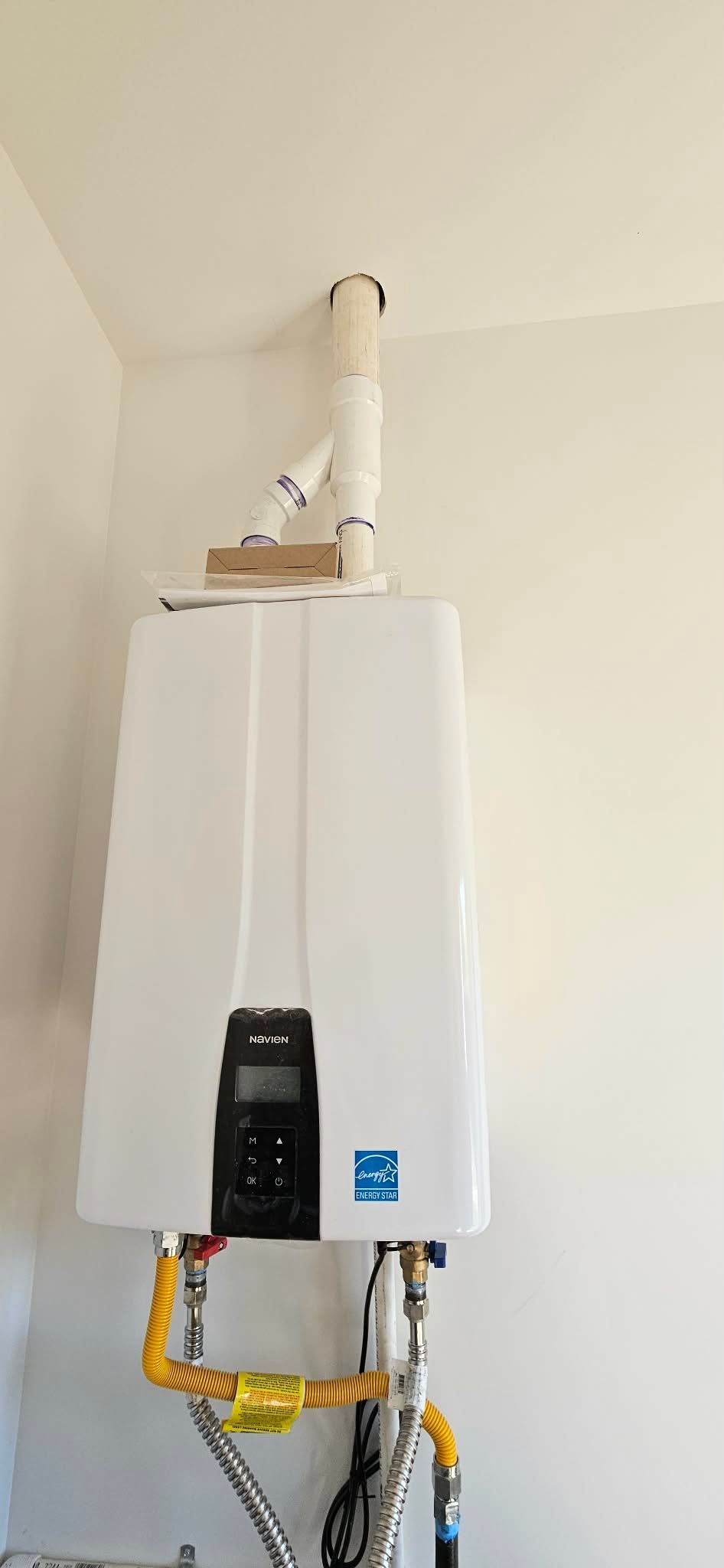 A white tankless water heater mounted on a wall with white PVC venting pipes connected to the top.