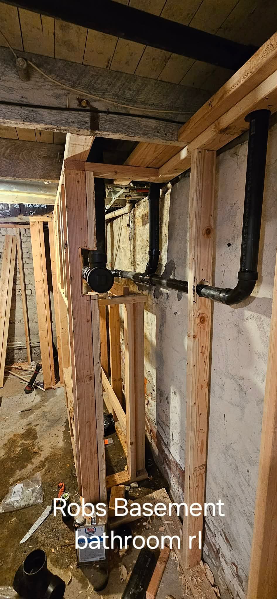 Exposed plumbing pipes installed in the wooden wall framing of a basement bathroom under construction.