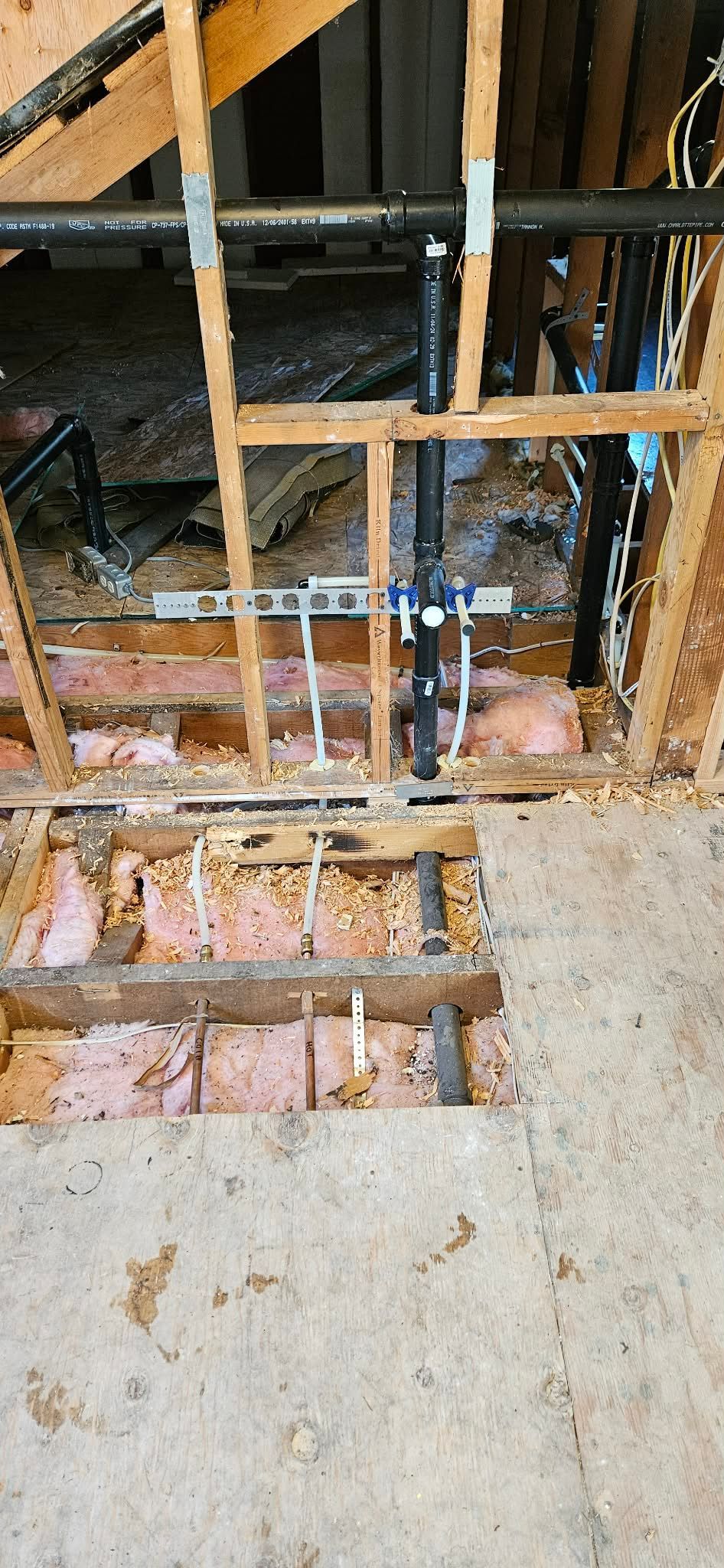 Plumbing work showing water lines and a metal bracket installed within the wooden framework of an unfinished wall.