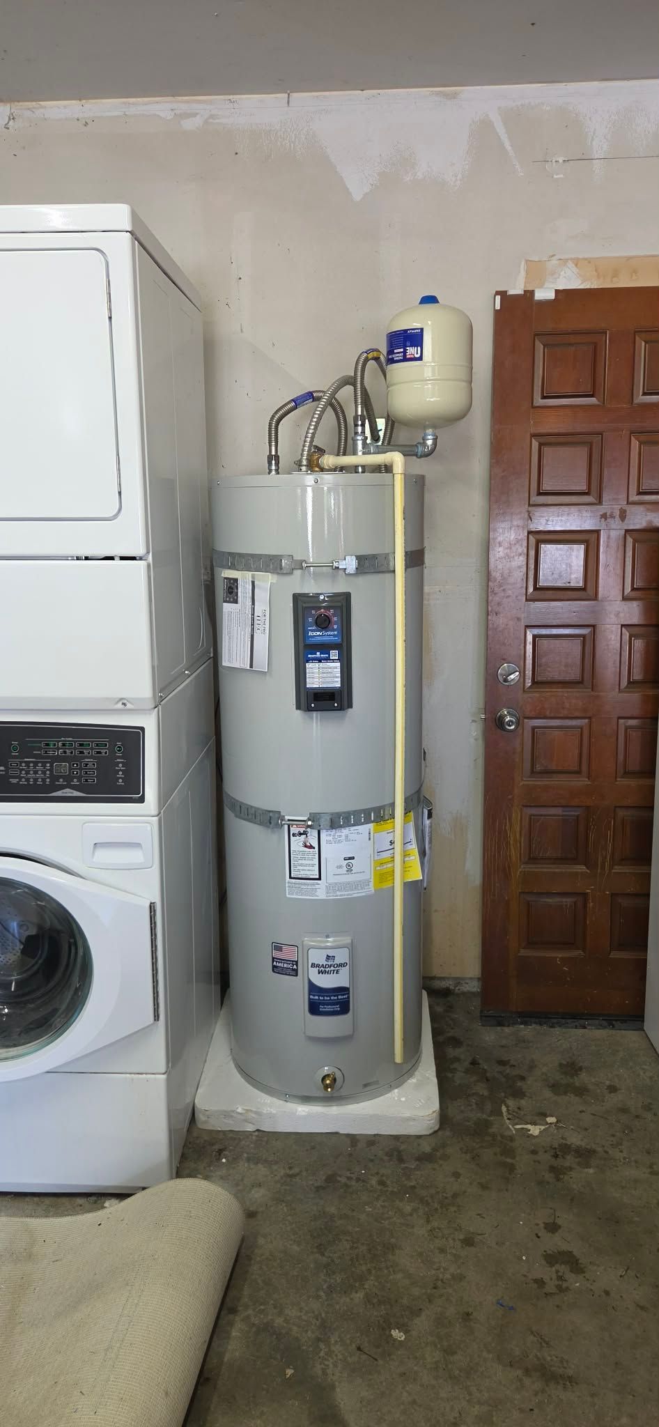 A white tankless water heater mounted on a wall with white PVC venting pipes connected to the top.