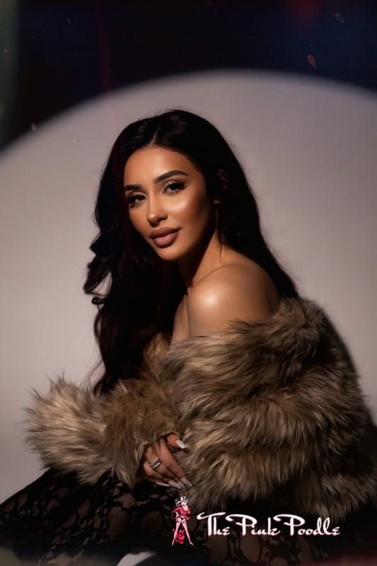 Portrait of a woman in a fur wrap, seated against a dark background with soft studio lighting