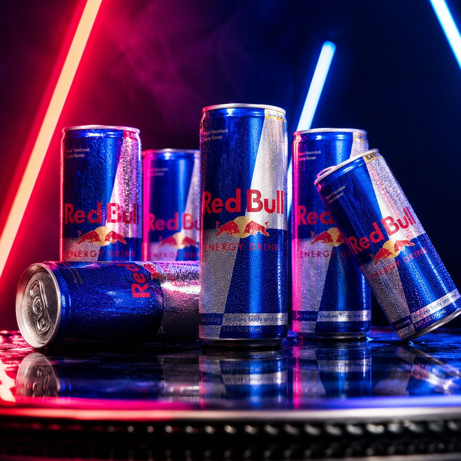 Assorted Red Bull cans in blue and silver, lit by neon red and blue lights on a reflective surface
