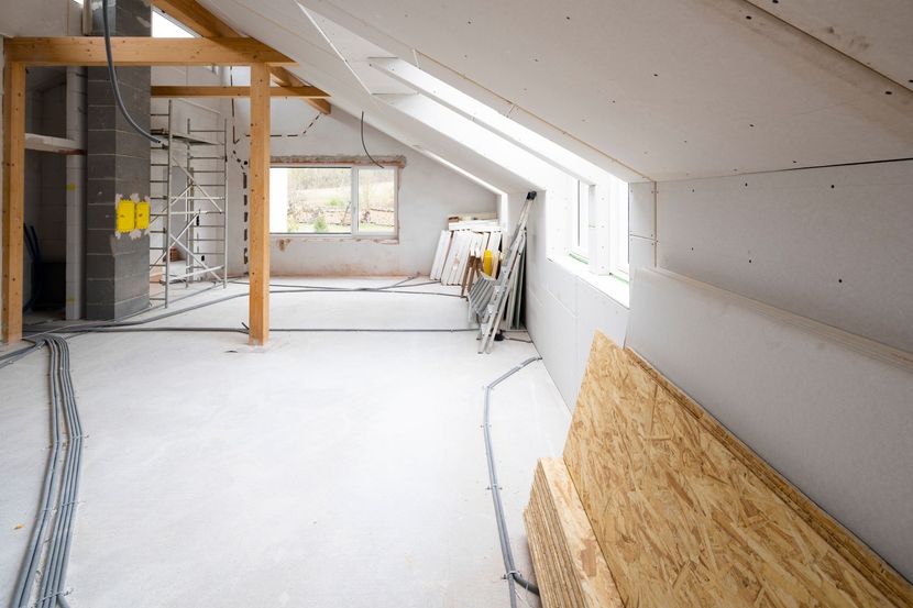 Interno di una stanza in costruzione; cartongesso nudo, cavi elettrici a vista, travi in legno e una finestra.