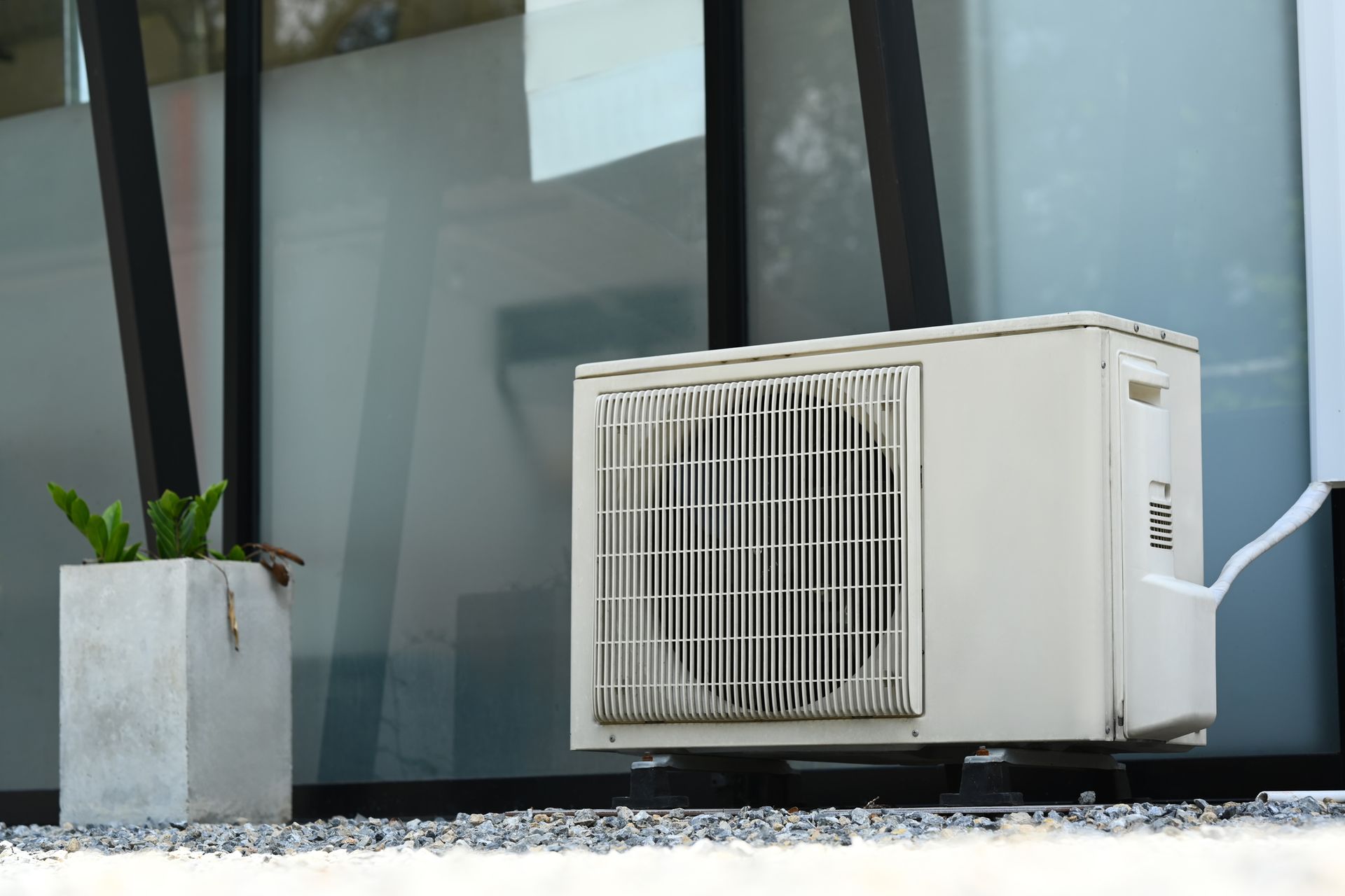 Un condizionatore bianco all'esterno di un edificio, accanto a una piccola pianta in un vaso di cemento.