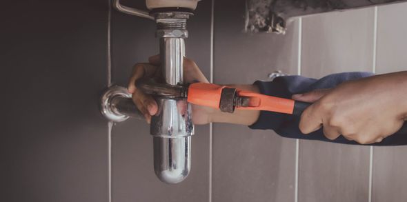 Una persona sta usando una chiave inglese arancione per riparare un tubo cromato del lavandino in un bagno.