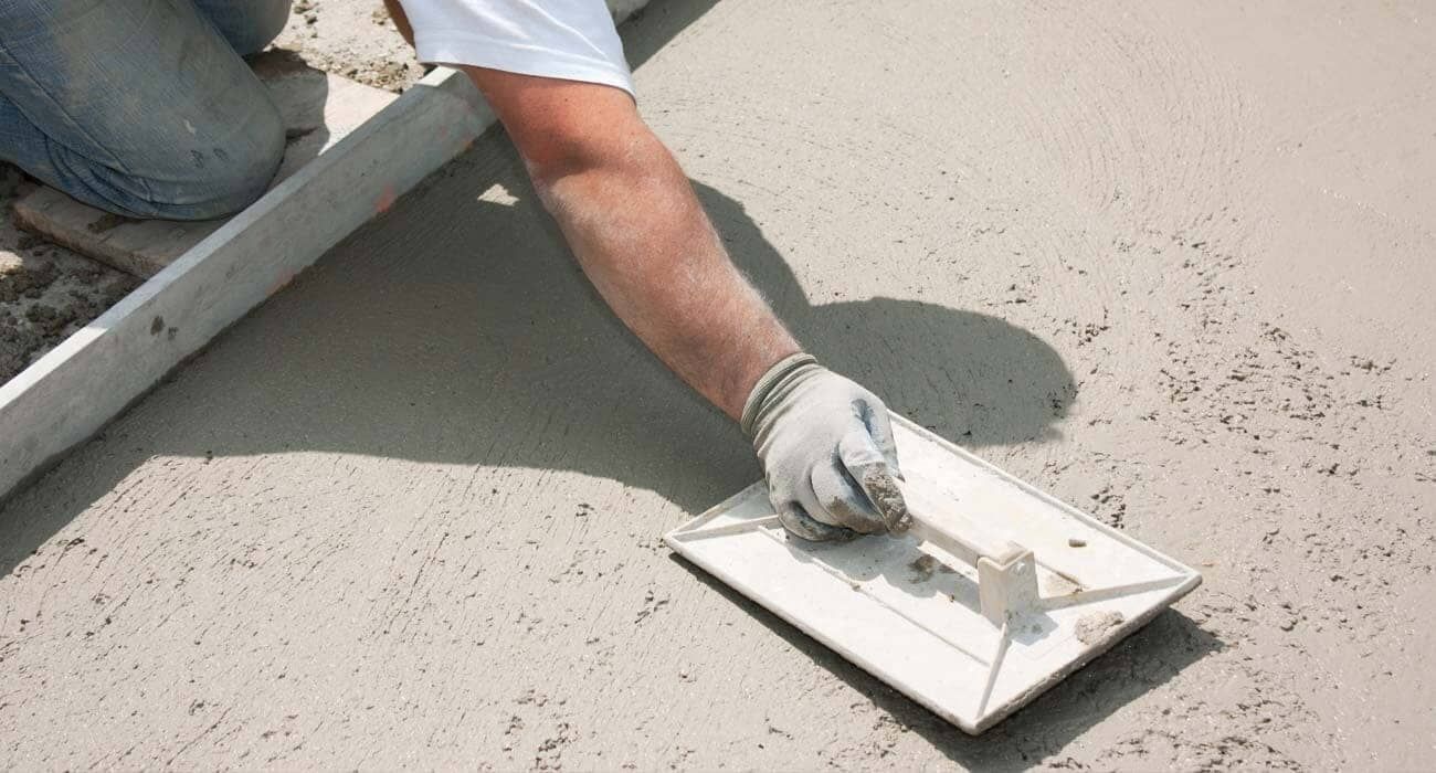 Persona que utiliza una paleta para alisar hormigón húmedo, al aire libre.