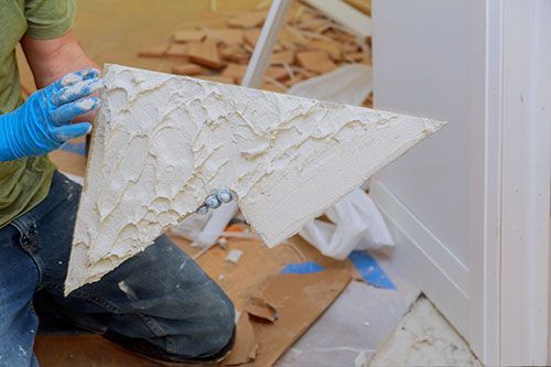 Una persona con guantes azules sostiene un material de construcción blanco, texturizado y en forma de triángulo.