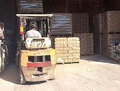 Operador de montacargas cargando sacos de cemento en un almacén. Se apilan palés con materiales.