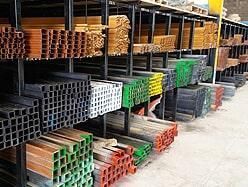 Estantes llenos de barras y tubos de metal de varios colores en un entorno de almacén.